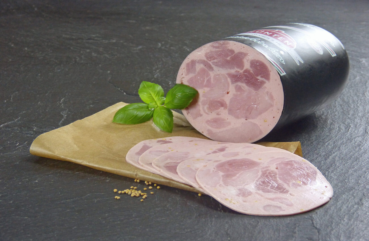 Bierschinken aufgeschnitten auf Backpapier und Kräutern angerichtet auf Schieferhintergrund