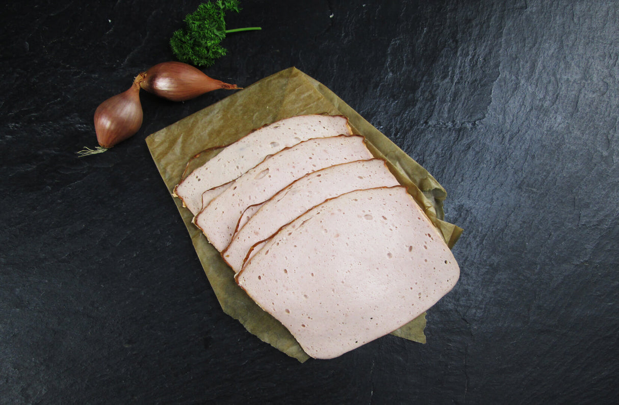 Fleischkäse gebacken geschnitten vom EIFEL Schwein mit Zwiebeln und Petersilie auf Schieferhintergrund