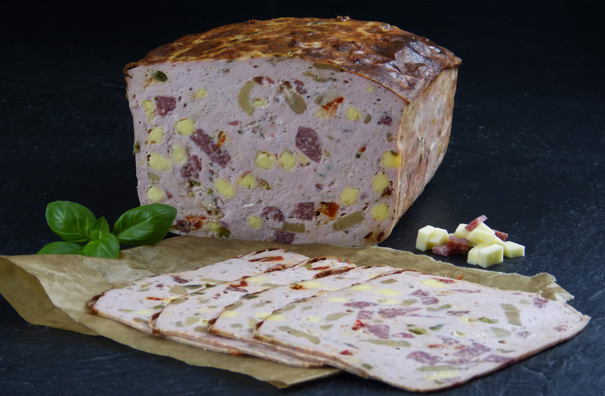 Pizzafleischkäse gebacken geschnitten vom EIFEL Schwein mit Basilikum Käsewürfeln und Salamiwürfeln auf Schieferhintergrund