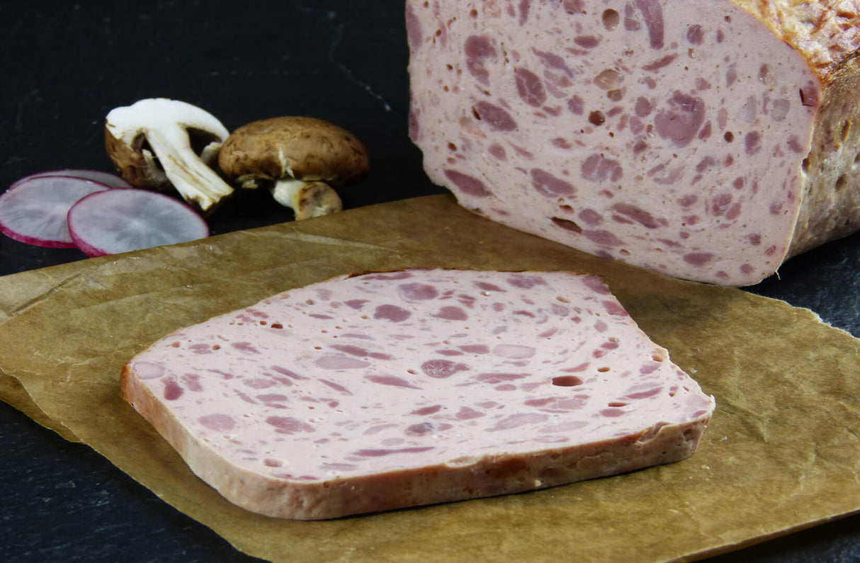 Fleischkäse grob gebacken Riegel vom EIFEL Schwein mit Radischenscheiben und Champignons auf Schieferhintergrund