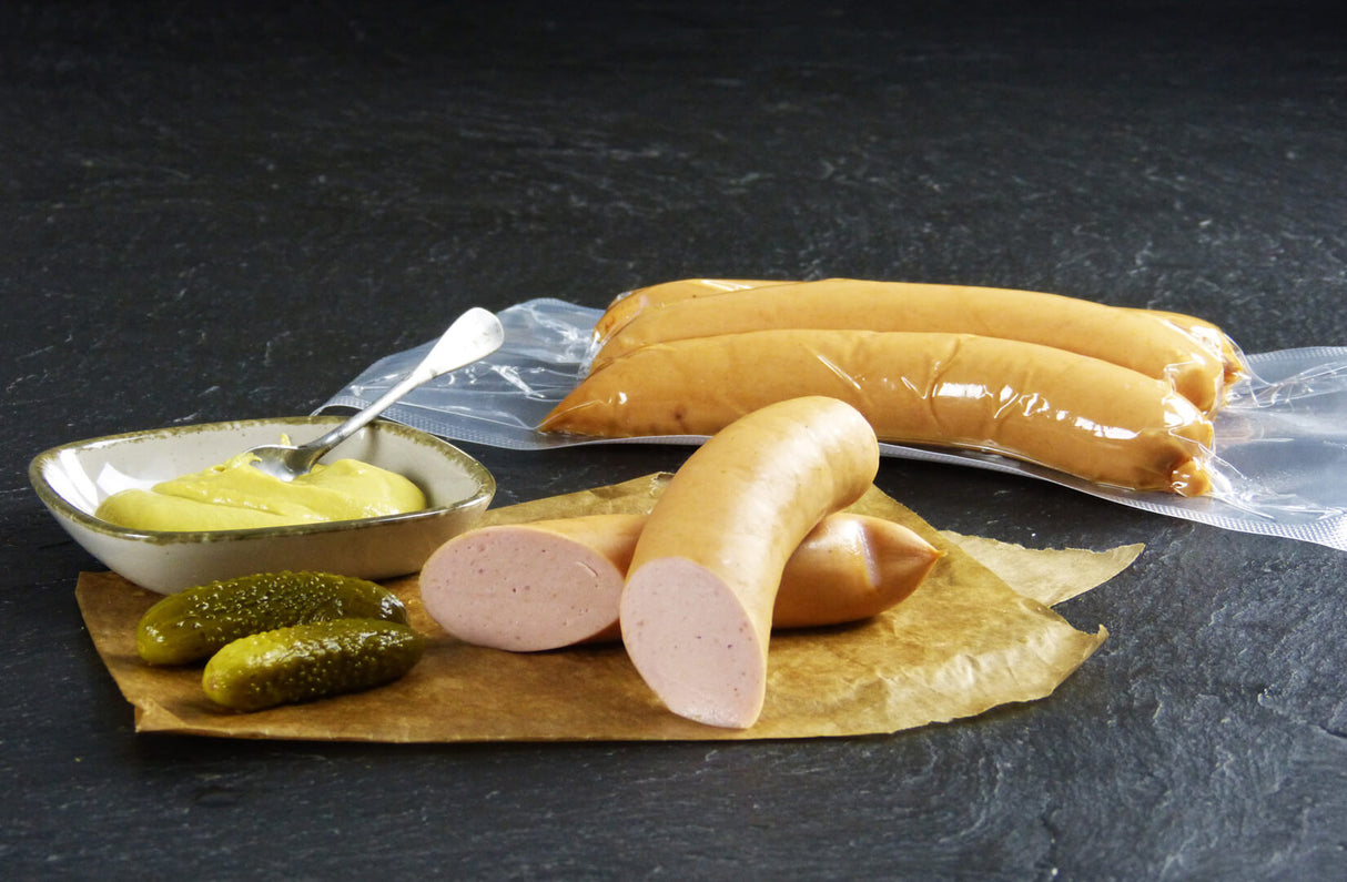 Fleischwürstchen vom EIFEL Schwein mit Gewürzgurken und einer Schüssel Senf auf Schieferhintergrund