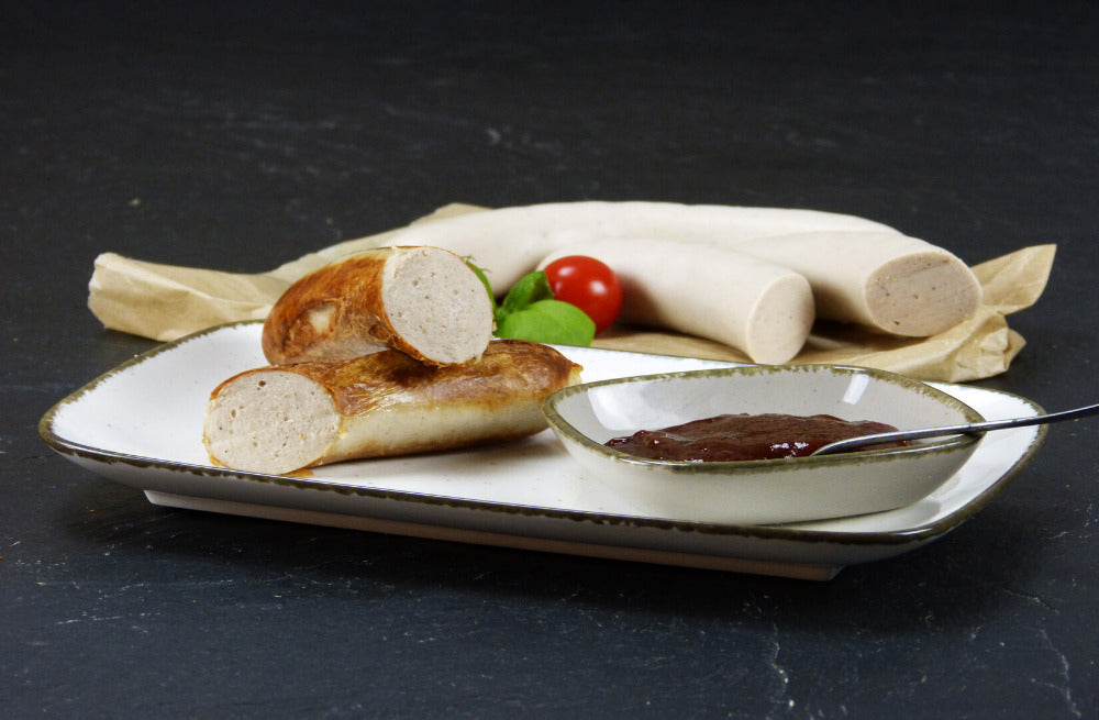 Bratwurst vom EIFEL Schwein mit einer Schüssel Gewürzketchup Basilikum und einer Cherrytomate auf Schieferhintergrund