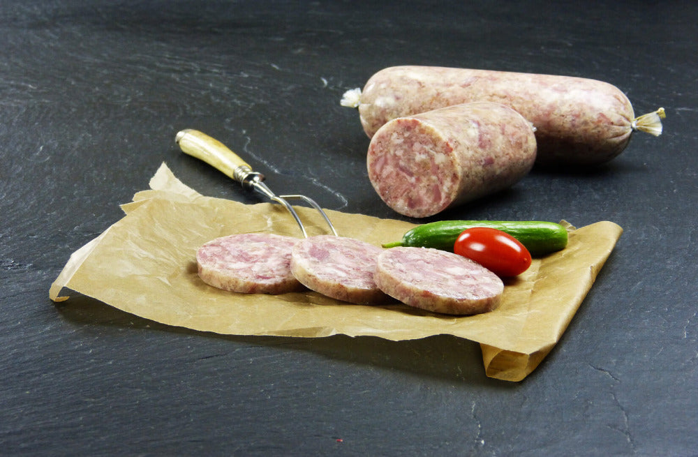 Hausmacher Schwartenmagen im Darm vom EIFEL Schwein mit Gurken und Cherry Tomaten auf Schieferhintergrund