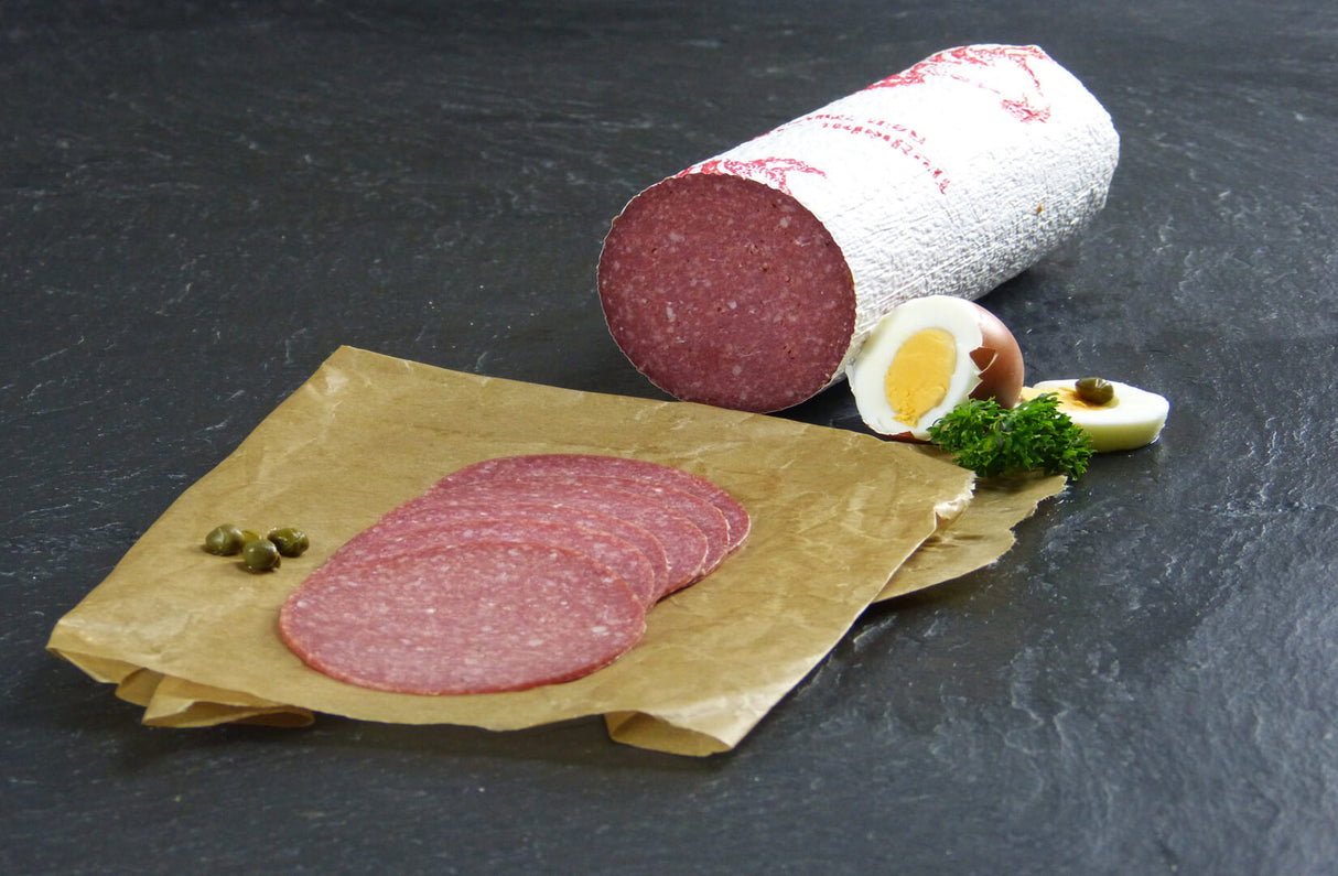 Putensalami geschnitten angerichtet auf Backpapier mit gekochtem Ei und Petersilie auf Schieferhintergrund