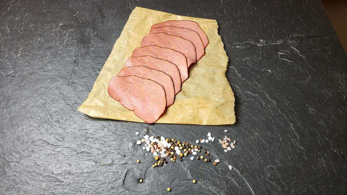Pastrami auf Backpapier angerichtet mit groben Salz und Pfefferkörnern auf Schieferhintergrund