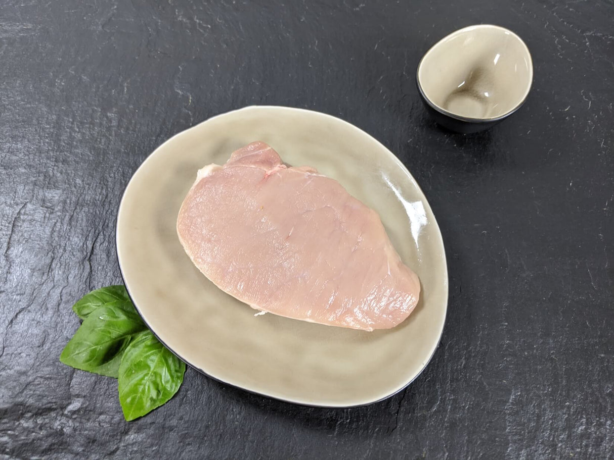 Schweinerückensteak natur auf Teller angerichtet mit Kräutern auf Schieferhintergrund