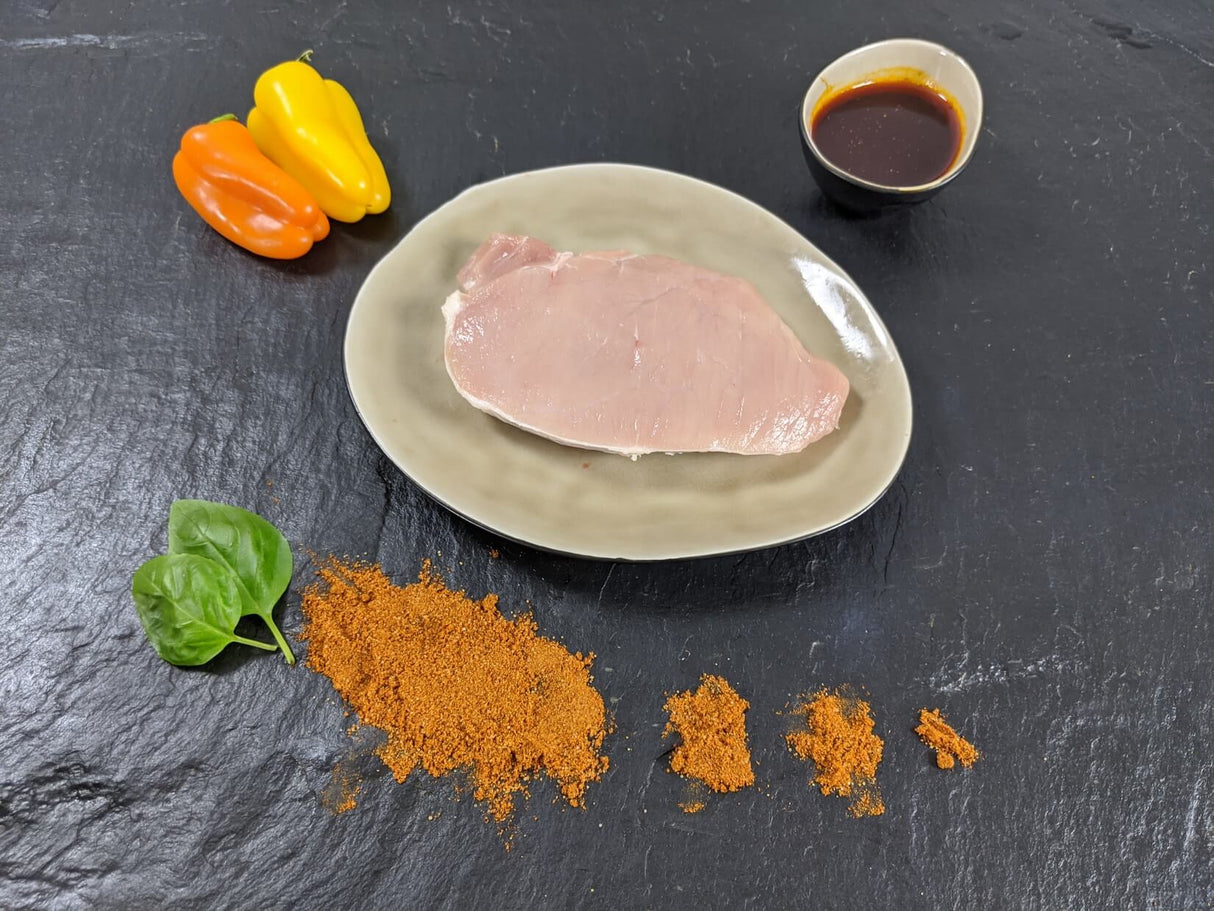 Schweinerückensteak Paprika auf Teller angerichtet mit einer Schale Marinade Paprikas Kräutern und Paprikapulver auf Schieferhintergrund