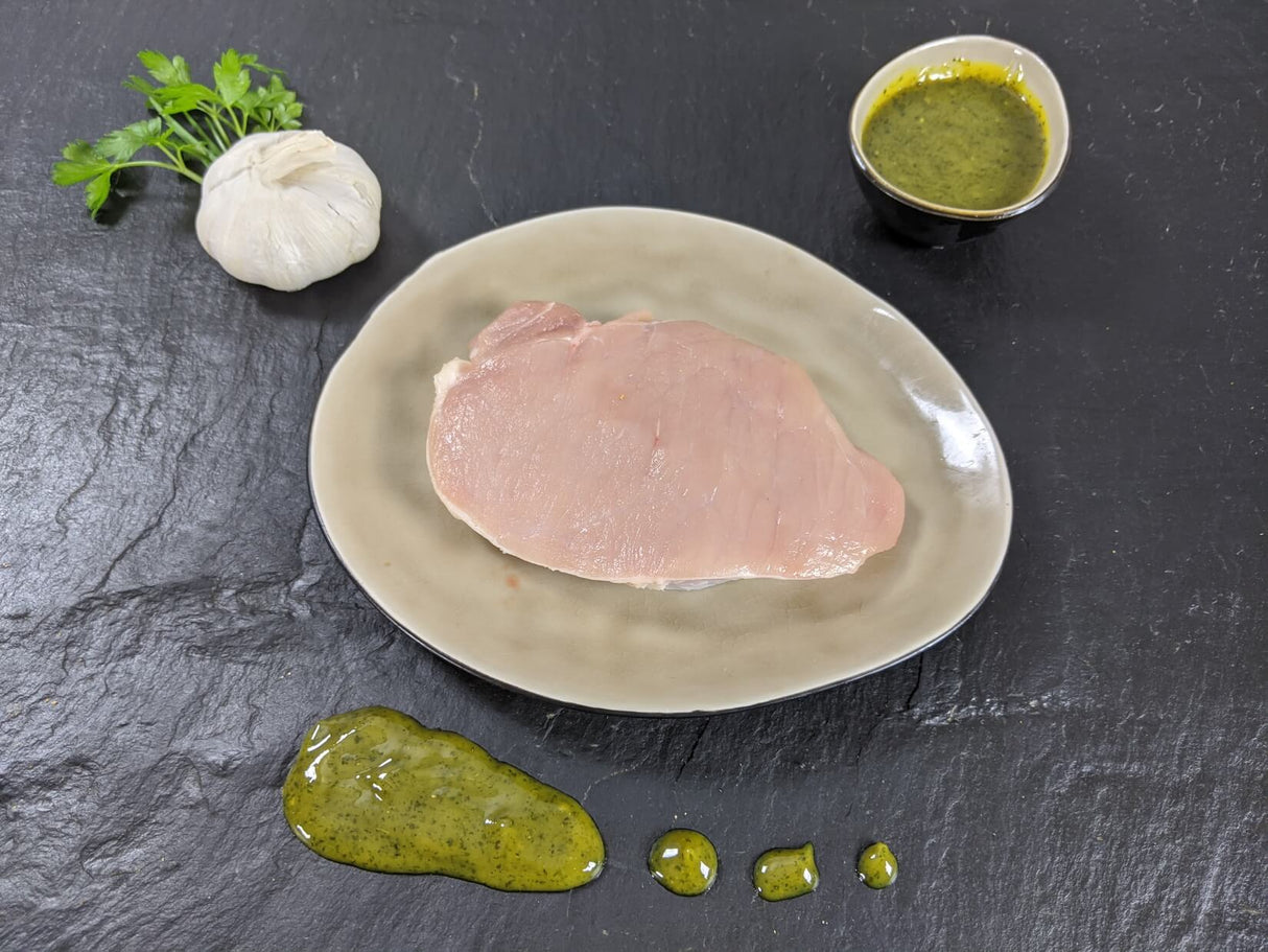 Schweinerückensteak Kräuter Knoblauch auf Teller angerichtet mit einer Schale Marinade, Knoblauchknollen und Kräutern