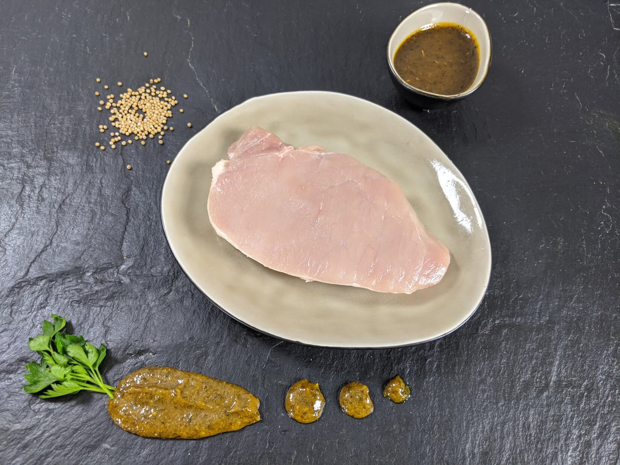 Schweinerückensteak Senfzauber auf Teller angerichtet mit einer Schale Senf Marinade Senfkörnern und Kräutern auf Schieferhintergrund