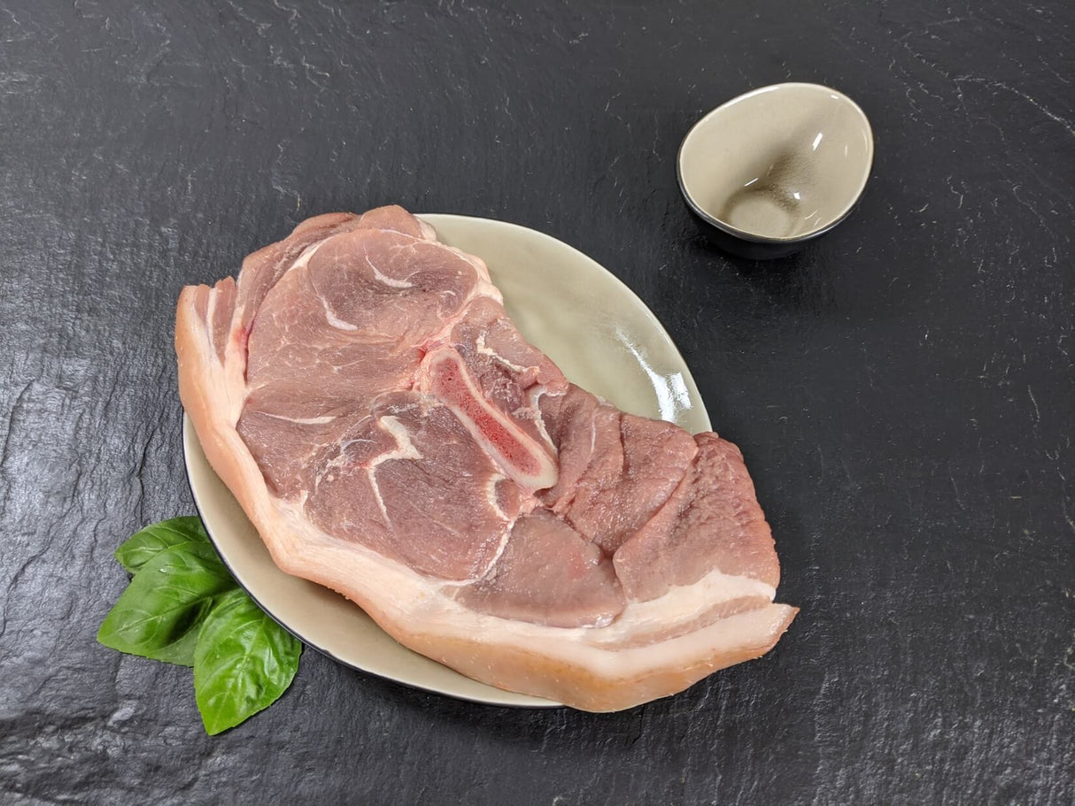 Holzfällersteak natur auf Teller angerichtet mit Kräutern auf Schieferhintergrund