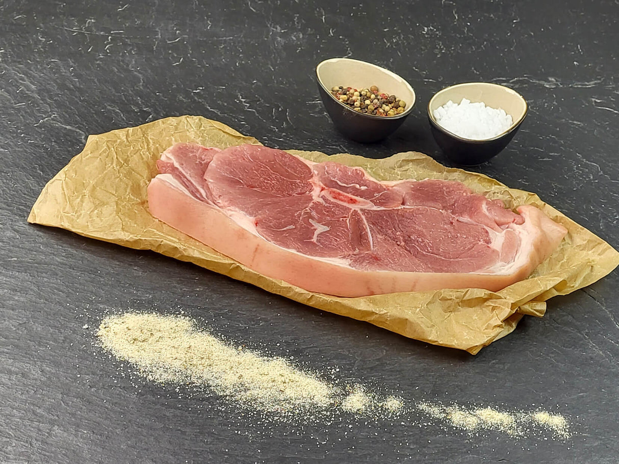 Holzfällersteak Pfeffer und Salz auf Backpapier angerichtet mit grobem Salz und Pfefferkörnern auf Schieferhintergrund