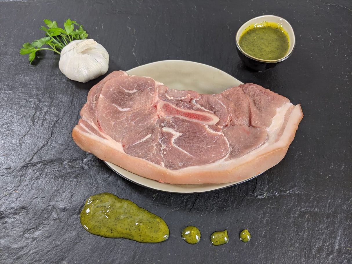 Holzfällersteak Kräuter Knoblauch auf Teller angerichtet mit einer Schale Marinade Knoblauchknolle und Kräutern auf Schieferhintergrund