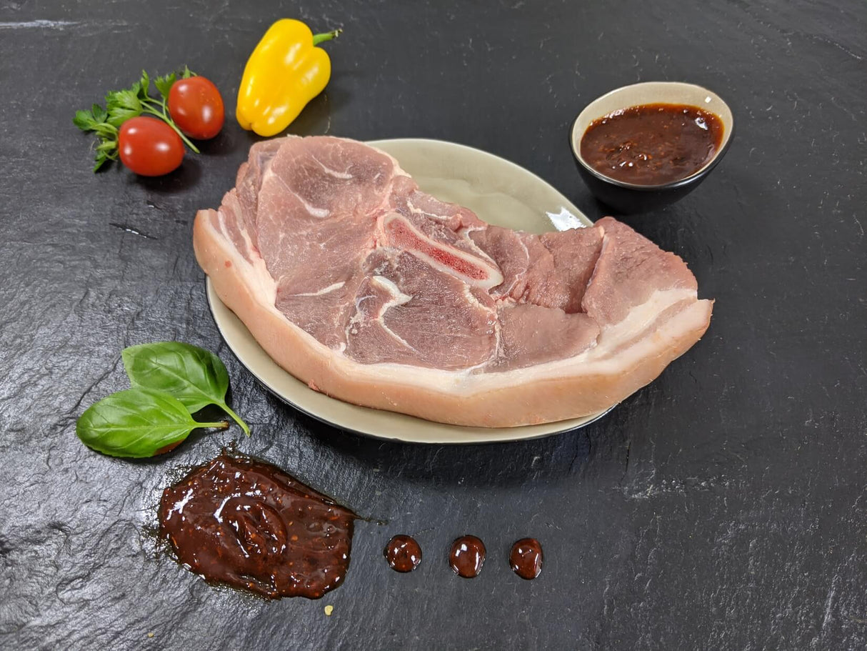 Holzfällersteak Barbecue auf Teller angerichtet mit einer Schale Marinade Tomaten und Kräutern auf Schieferhintergrund