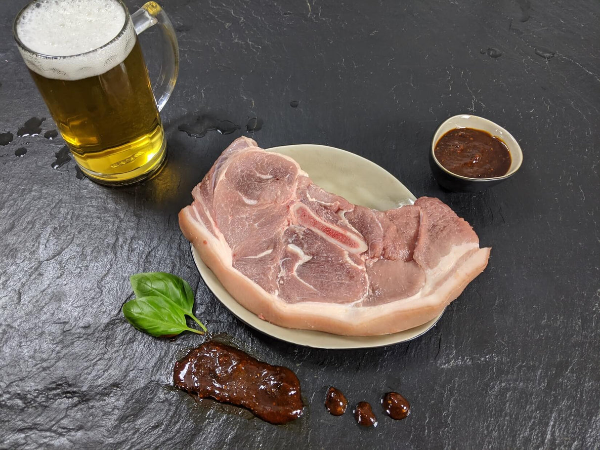 Holzfällersteak Braumeister auf Teller angerichtet mit einer Schale Marinade Kräutern und einem Glas Bier auf Schieferhintergrund