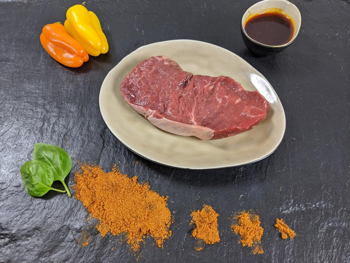 Rumpsteak Paprika auf Teller angerichtet mit einer Schale Marinade Paprika Kräutern und Paprikapulver auf Schieferhintergrund