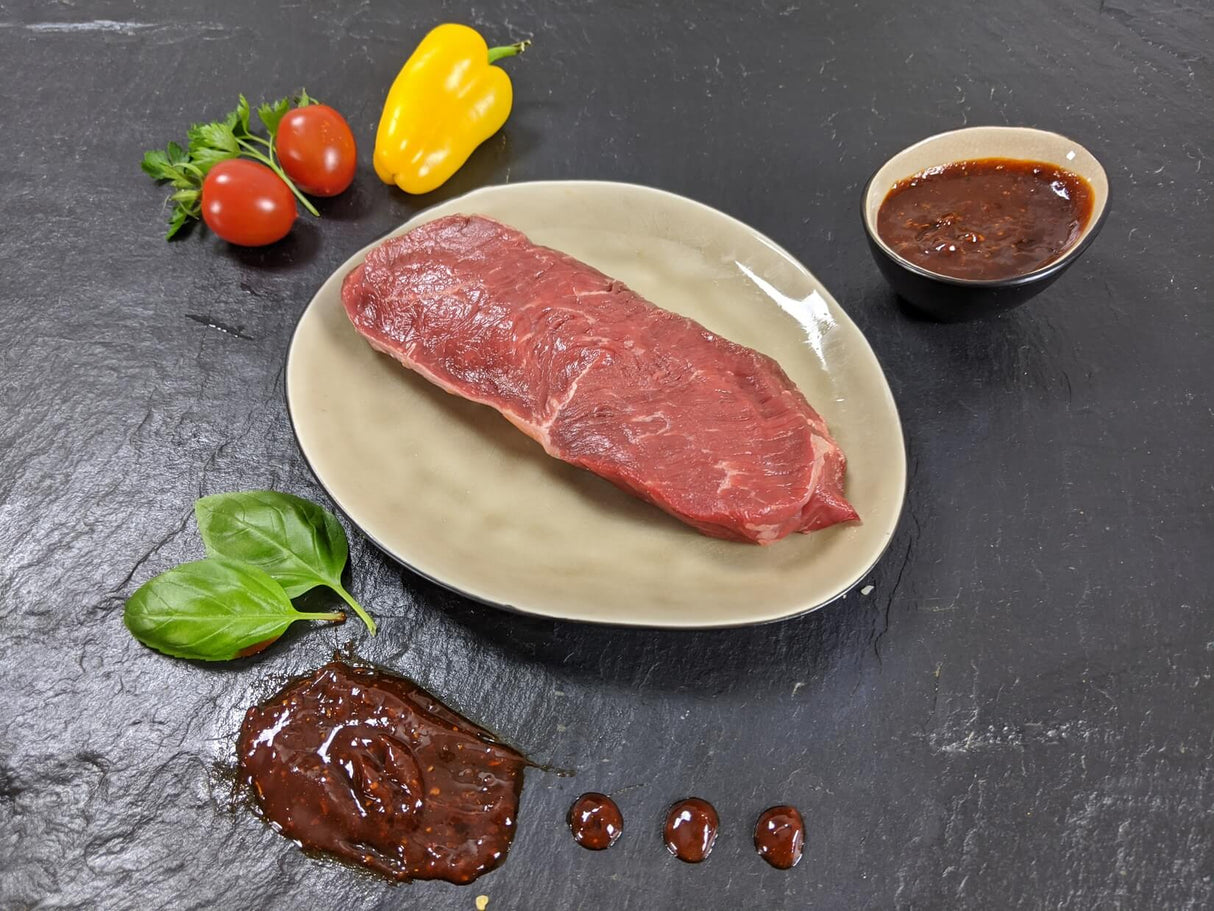 Rumpsteak Barbecue auf Teller angerichtet mit einer Schale Marinade Tomaten Paprika und Kräutern auf Schieferhintergrund