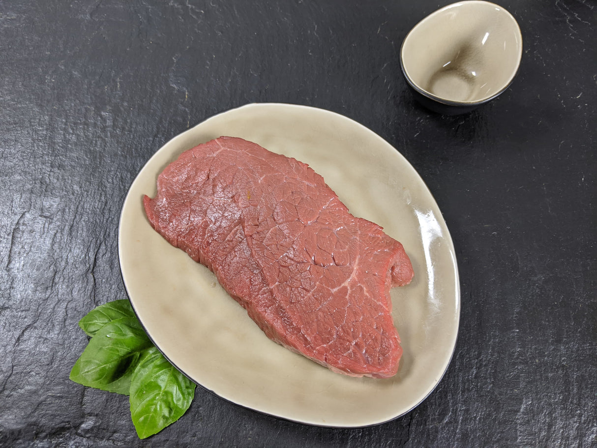 Rinderhüftsteak natur auf Teller angerichtet mit Kräutern auf Schieferhintergrund