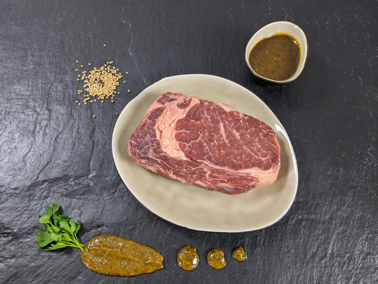 Entrecôte Senfzauber auf Teller angerichtet mit einer Schale Marinade Senfkörnern und Kräutern auf Schieferhintergrund