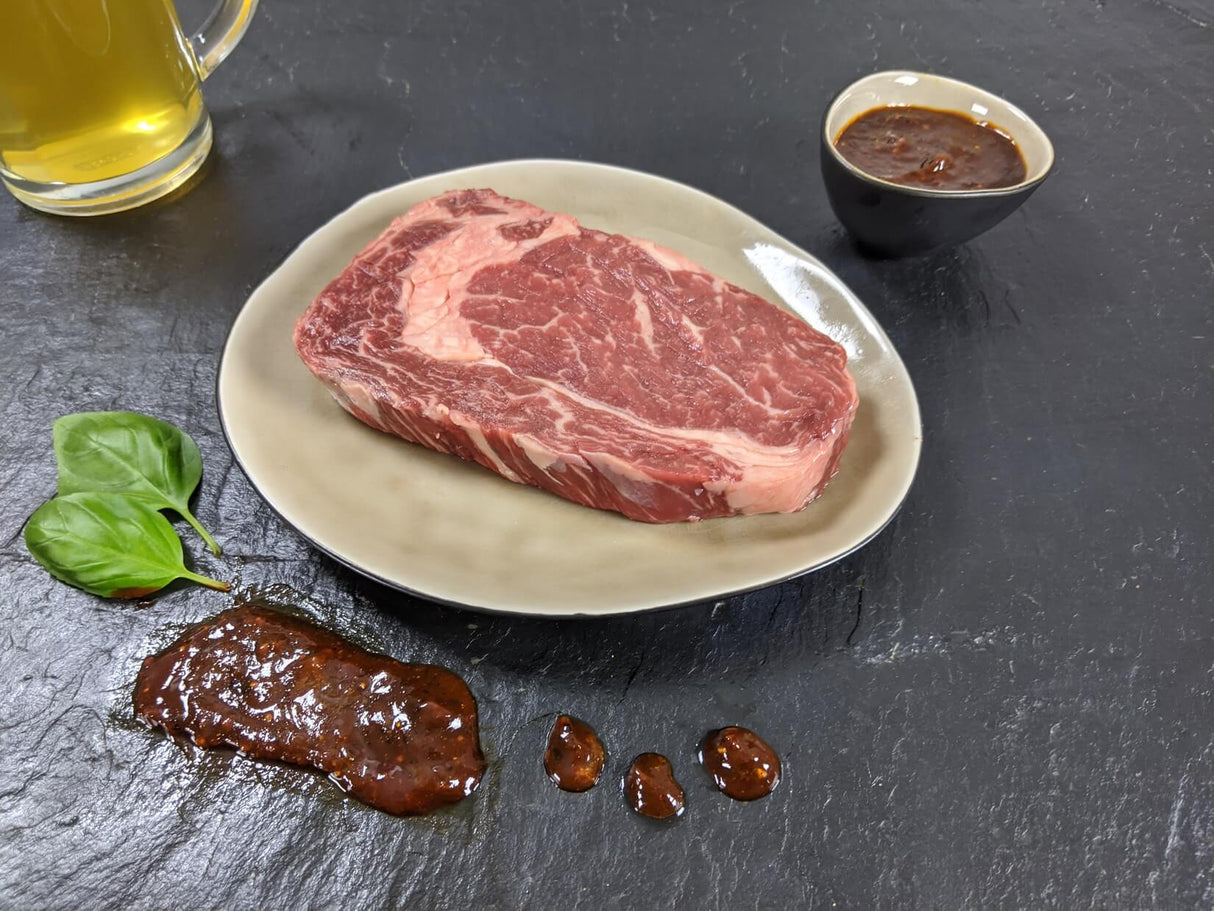 Entrecôte Braumeister auf Teller angerichtet mit einer Schale Marinade Kräutern und einem Glas Bier auf Schieferhintergrund