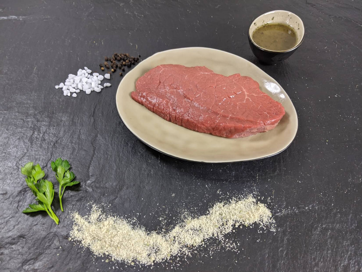 Rinderhüftsteak Pfeffer und Salz auf Teller mit einer Schale Marinade grobem Salz und Pfefferkörnern und Kräutern auf Schieferhintergrund