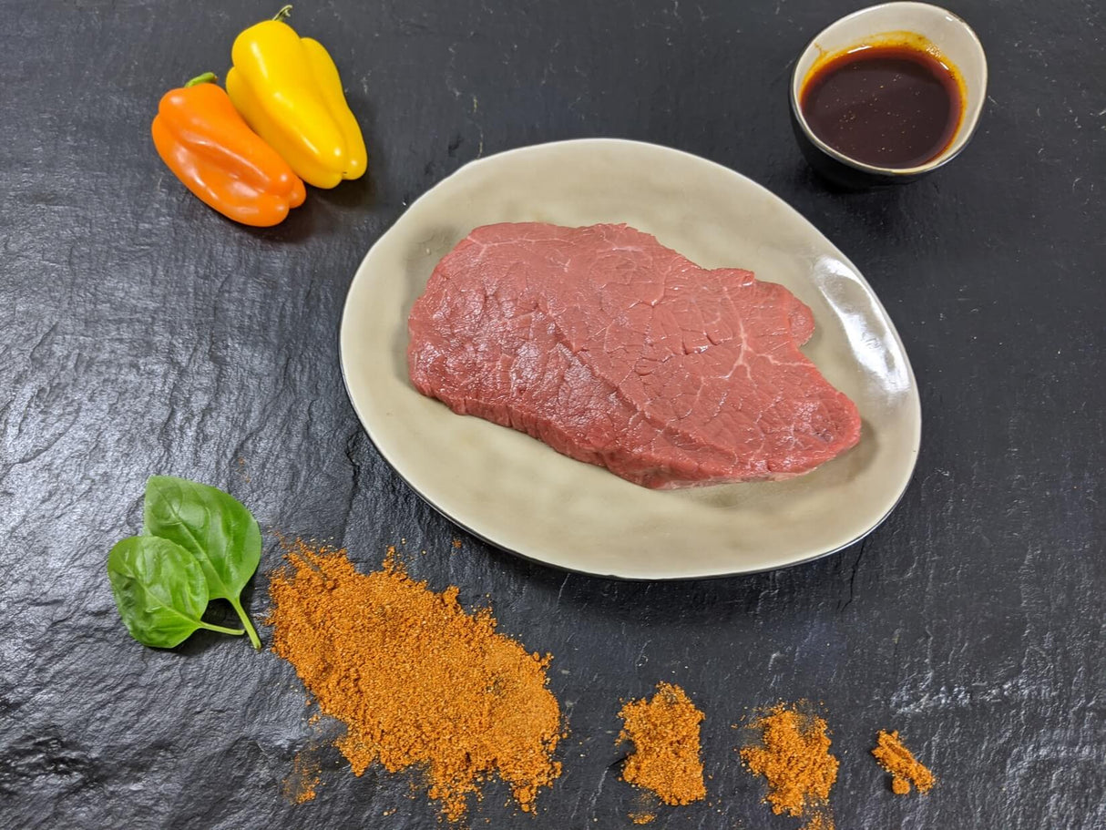 Rinderhüftsteak Paprika auf Teller angerichtet mit einer Schale Marinade Paprika Kräutern und Paprikapulver auf Schieferhintergrund