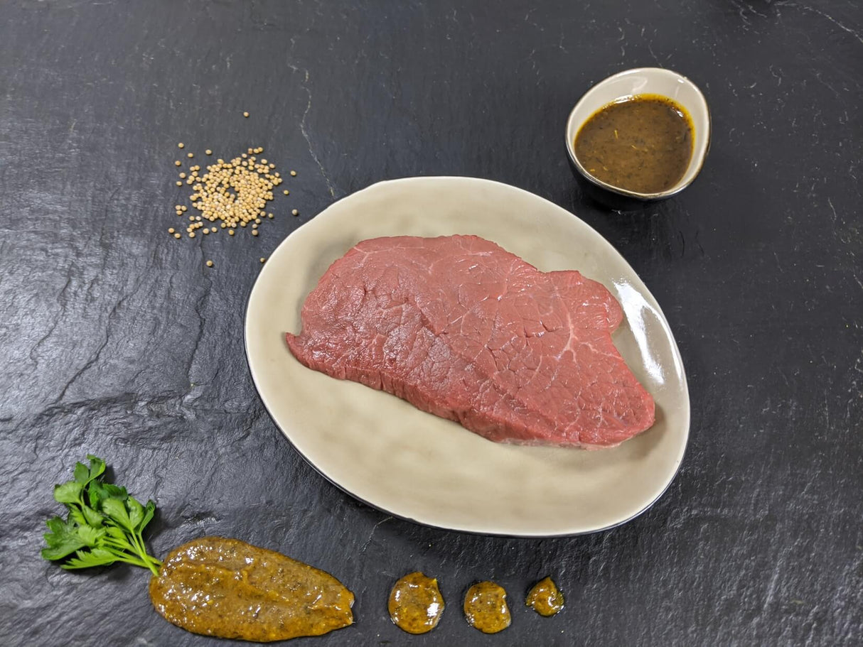 Rinderhüftsteak Senfzauber auf Teller angerichtet mit Schale Marinade Senfkörnern und Kräutern auf Schieferhintergrund