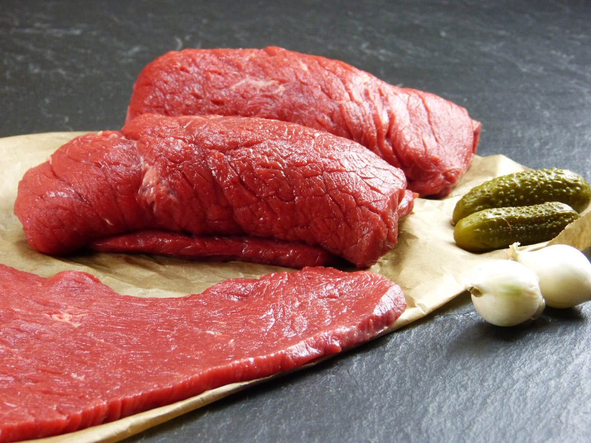 Rinder Rouladen aus der Oberschale gerollt auf Backpapier angerichtet mit Essiggurken und Silberzwiebeln auf Schieferhintergrund