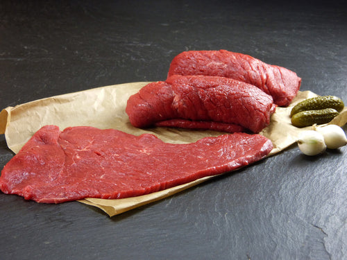 Rinder Rouladen aus der Oberschale auf Backpapier angerichtet mit Essiggurken und Silberzwiebeln auf Schieferhintergrund