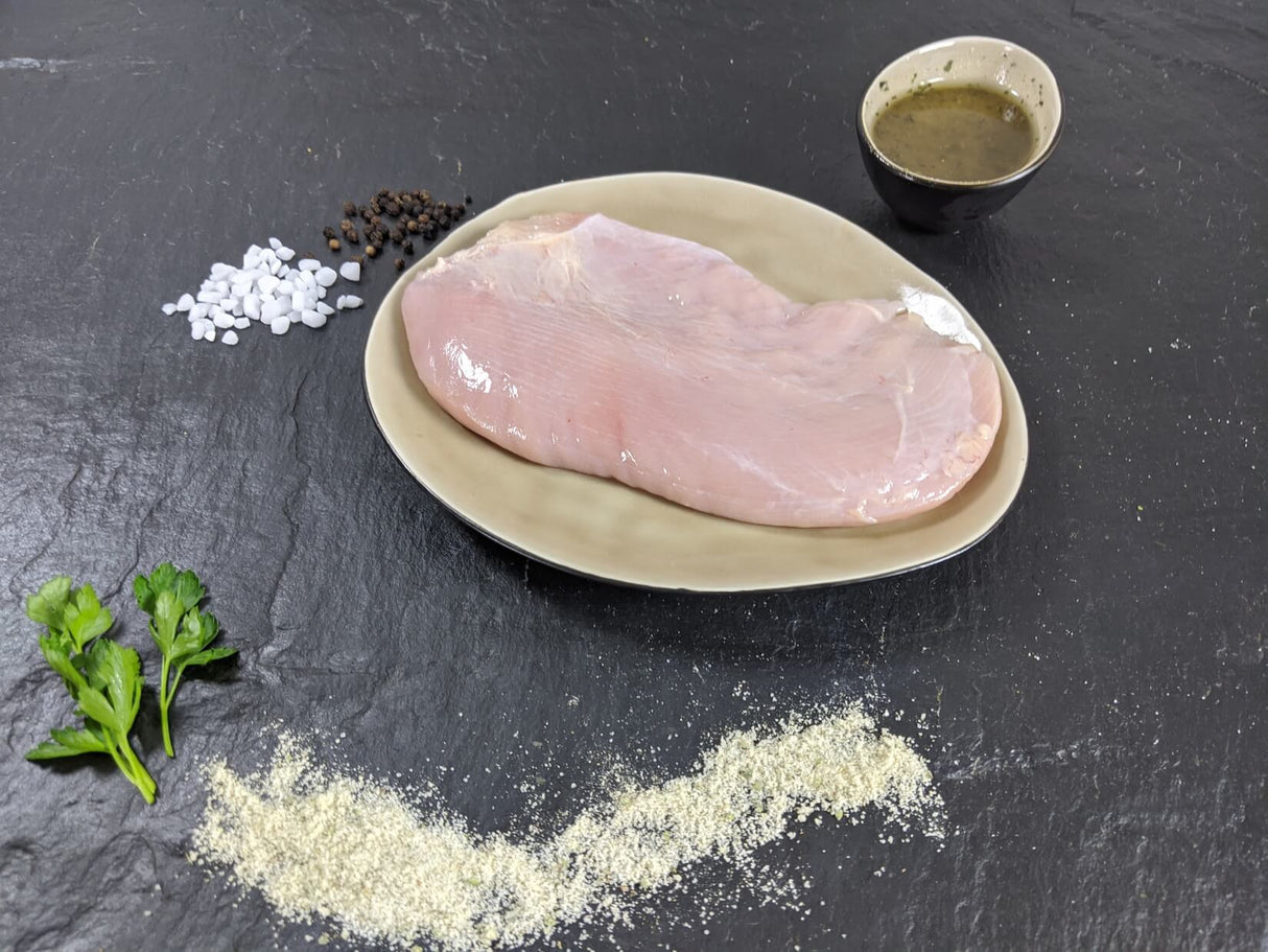 Putensteak Pfeffer und Salz auf Teller angerichtet mit einer Schale Marinade groben Salz und Pfefferkörnern und Kräutern auf Schieferhintergrund