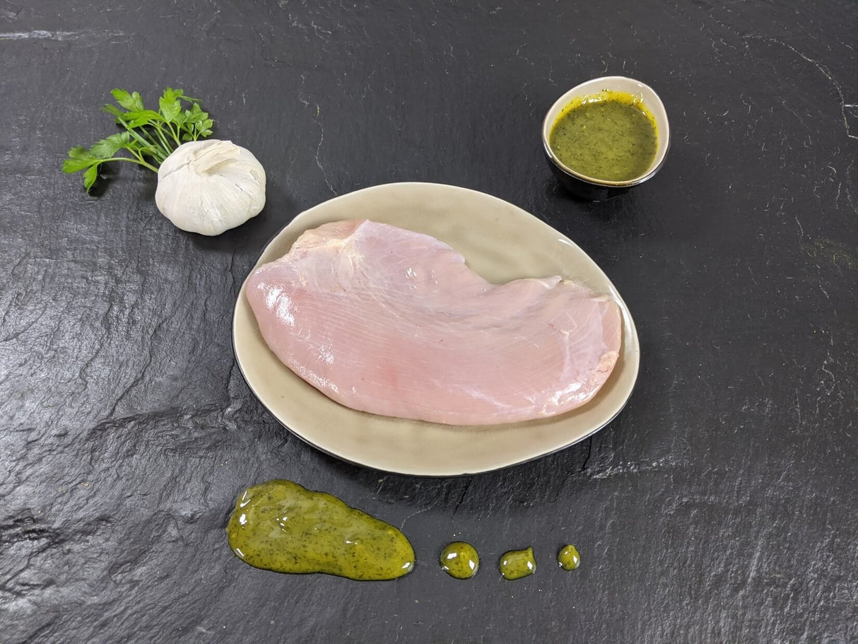 Putensteak Natur auf Teller angerichtet mit einer Schale Kräuter Knoblauch Marinade mit Petersilie einer Knoblauchzehe auf Schieferhintergrund