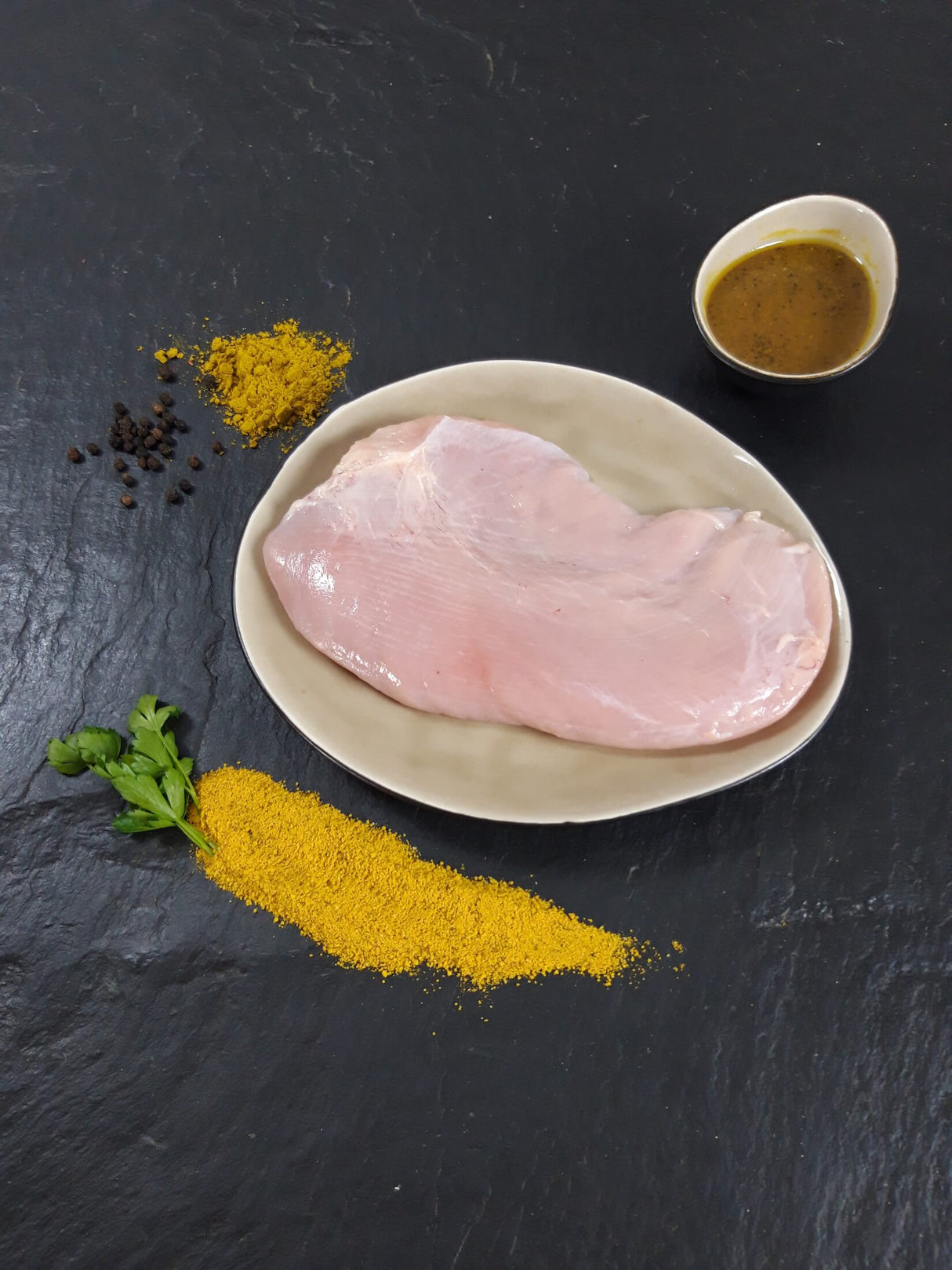 Putensteak Bombay auf Teller angerichtet mit einer Schale Bombay Marinade Gewürzen und Kräutern