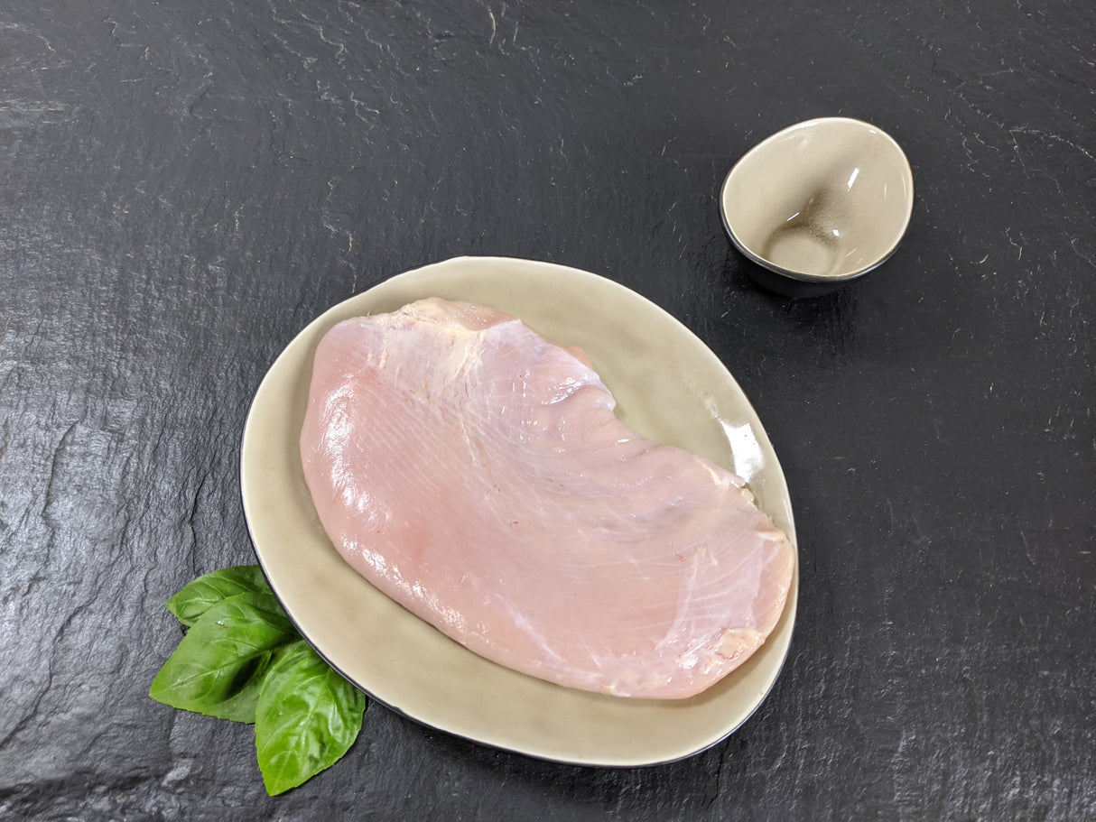 Putensteak natur auf Teller angerichtet mit Kräutern auf Schieferhintergrund