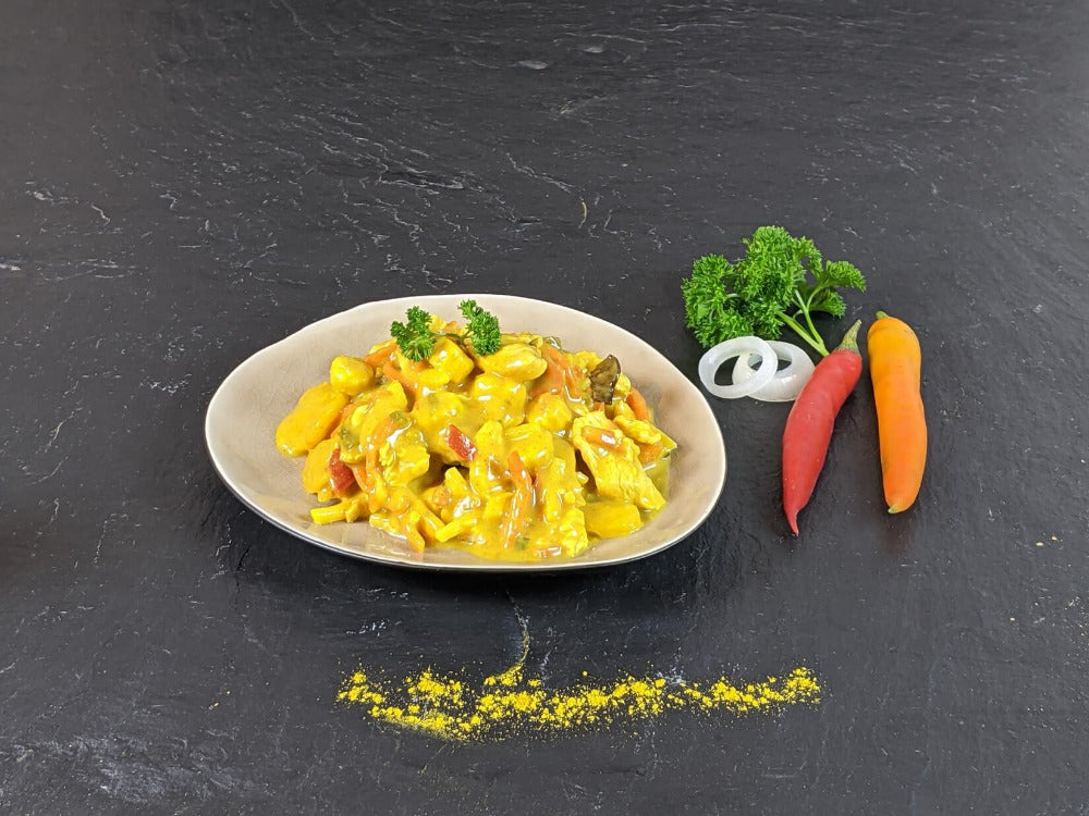 Puten Curry auf Teller angerichtet mit Petersilie Zwiebeln und Chilischoten auf Schieferhintergrund