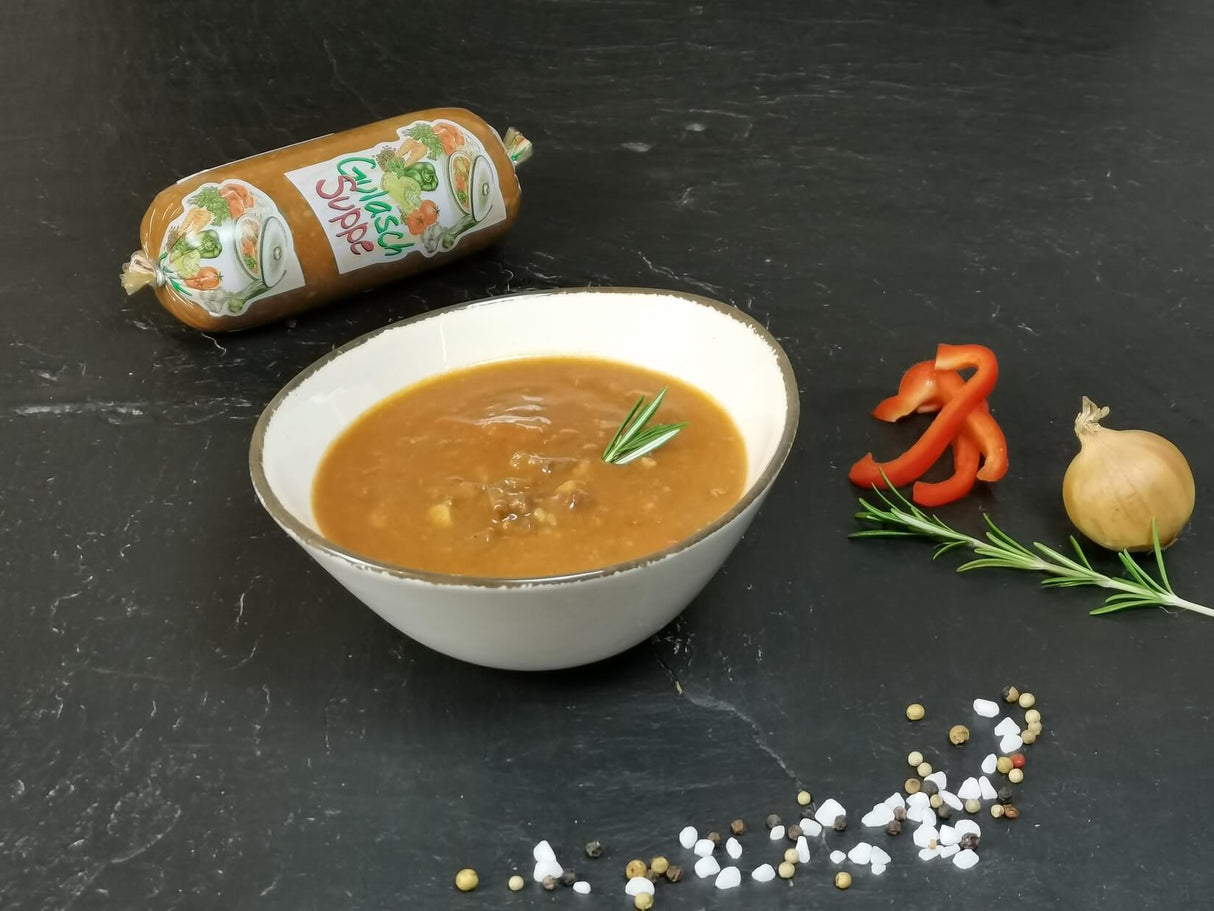 Gulaschsuppe in Schale angerichtet mit Paprika Zwiebel und Rosmarin auf Schieferhintergrund