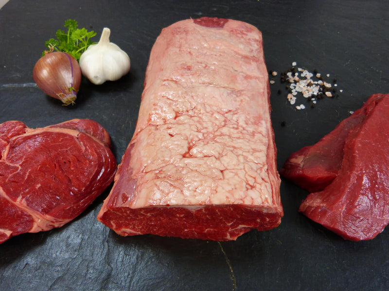 Alles vom argentinischen Rind Steak Paket Auswahl aus Argentinischem Roastebef Entrecote und Hüftsteaks auf Schieferhintergrund serviert mit Zwiebel Knoblauchknolle, Petersilie und Salzkörnern
