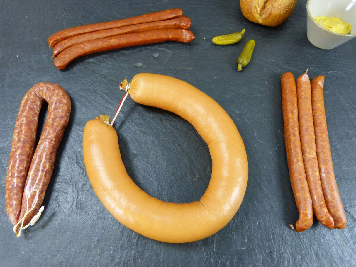 Wanderpaket mit Fleischwurst Rohessern luftgetrockneter Mettwurst mit Senf Brötchen und Gewürzgurken dekoriert auf Schieferhintergrund