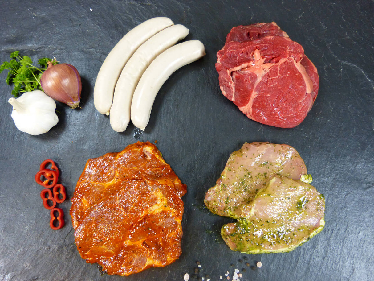 Drei Bratwürstchen ein Entrecote Steak ein Kammsteak Barbecue und ein Rückensteak Paprika auf Schieferhintergrund