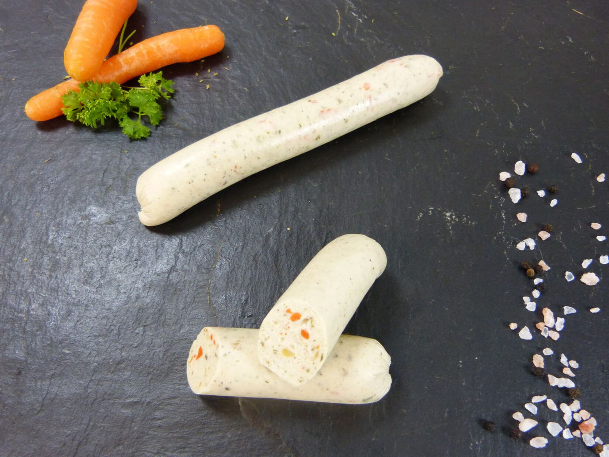 Vegetarische Bratwurst auf Schieferhintergrund angerichtet mit Karotte Kräutern und groben Salz und Pfefferkörnern