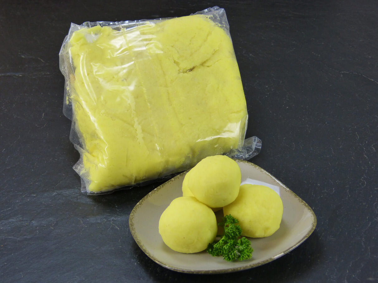 Kloßteig frisch im Beutel und drei geformten Klößen auf Teller vor Schieferhintergrund