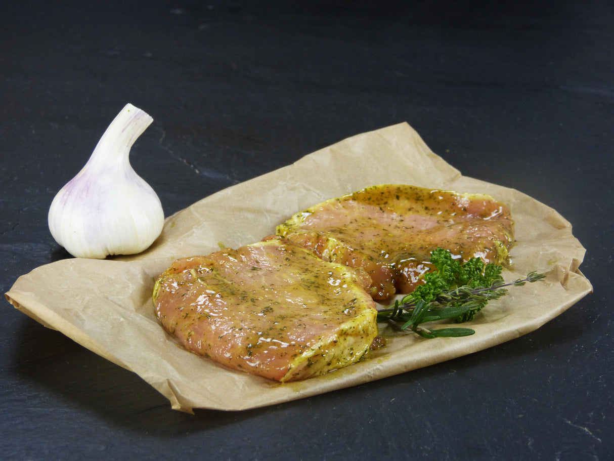 Schweinerückensteak Kräuter Knoblauch angerichtet auf Backpapier mit Knoblauchknolle und Kräutern auf Schieferhintergrund