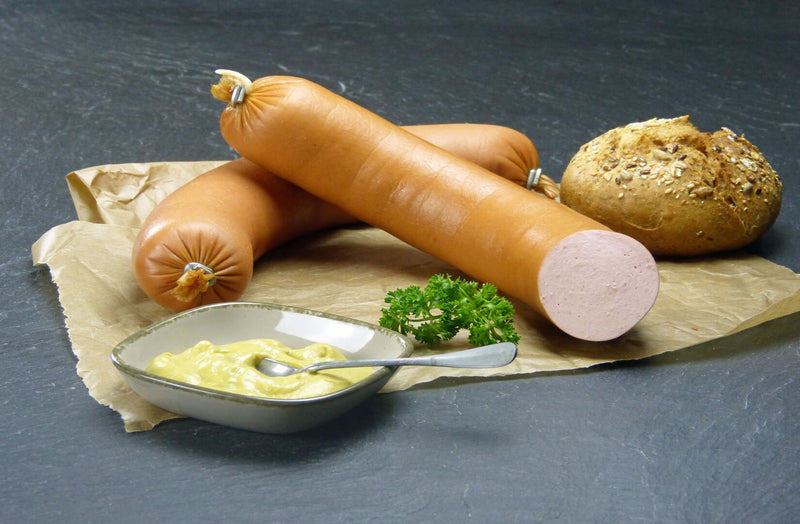 EIFEL Schwein Fleischwurst im Ring auf Backpapier mit Petersilie einer Schale Senf und einem Körnerbrötchen auf Schieferhintergrund