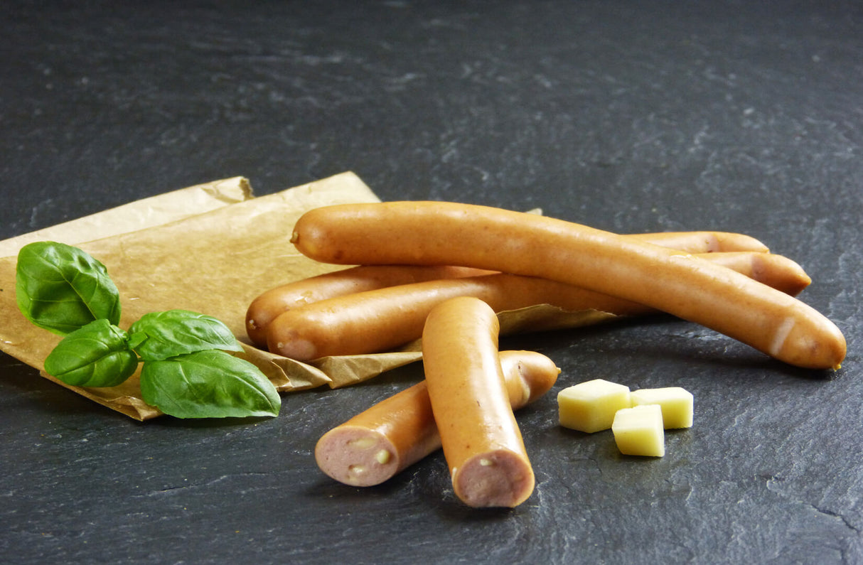 Käsewiener vom EIFEL Schwein auf Backpapier angerichtet mit Käsewürfeln und Kräutern auf Schieferhintergrund