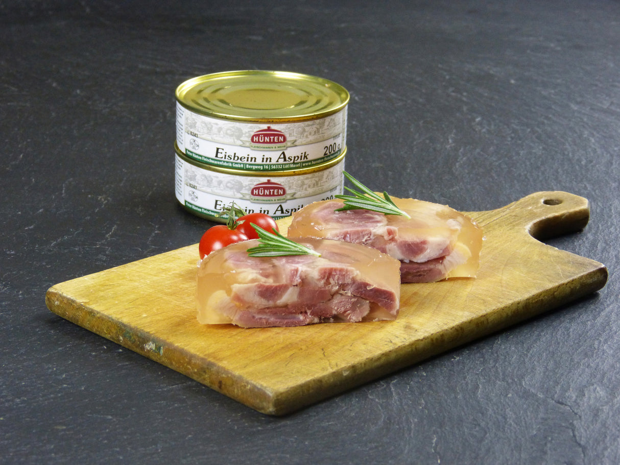 Eisbein in Aspik auf Holzbrett angerichtet mit Cocktailtomaten und Rosmarin auf Schieferhintergrund