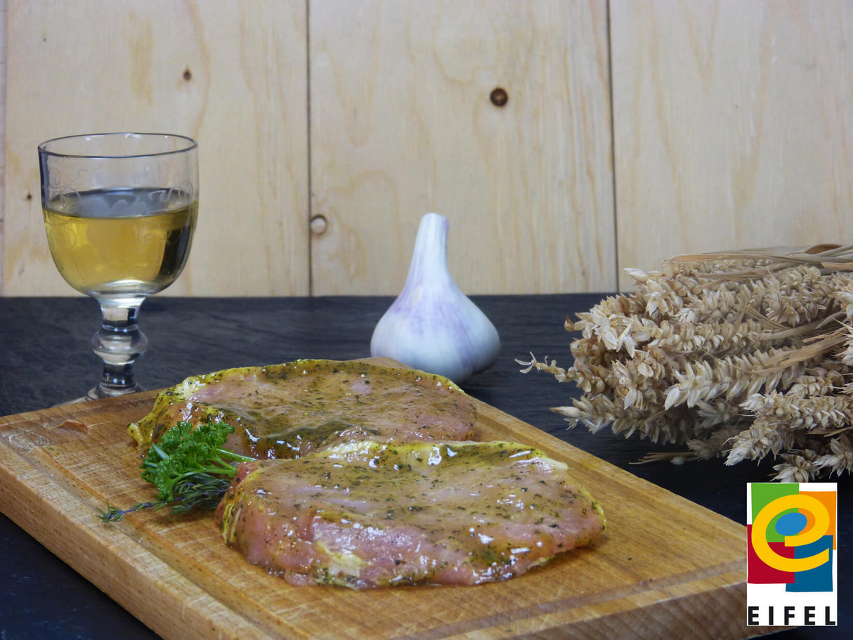 Rückensteak Kräuter Knoblauch vom EIFEL Schwein auf Holzbrett angerichtet mit Kräutern und Knoblauchknolle auf Schieferhintergrund