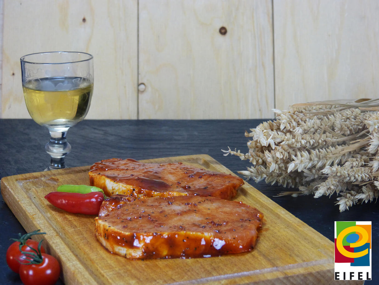 Rückensteak Barbecue vom EIFEL Schwein auf Holzbrett angerichtet mit Chilischoten auf Schieferhintergrund