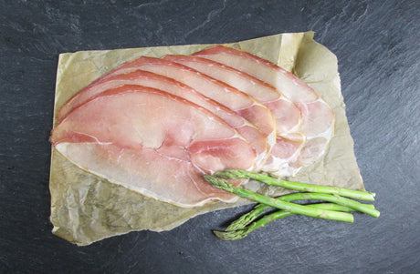 Rohschneider in Scheiben geschnitten angerichtet auf Backpapier mit grünem Spargel auf Schieferhintergrund