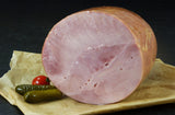 Gekochter Hinterschinken angerichtet mit eingelegten Gurken und einer Tomate auf Backpapier mit Schieferhintergrund