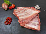 Spareribs von der Brustspitze roh mit Paprika und Zwiebeln sowie Gewürzen auf Schiefer
