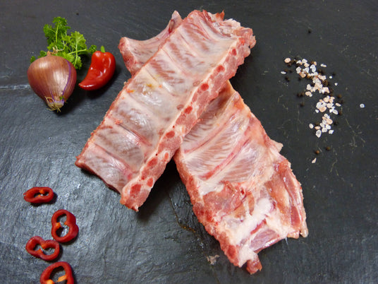 Kotelett Rippchen Spareribs frisch am Stück mit Paprika und  Zwiebeln mit Pfferkörnern und Petersilie auf Schieferhintergrund