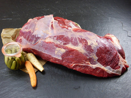 Dickes Bugstück vom EIFEL Rind angerichtet mit Sellerie einer Karotte und einem Gewürzgurkenglas auf Backpapier mit Schieferhintergrund